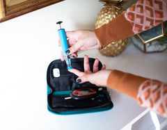 The Genteel Lancing Device being used for a finger print test with a travel pouch and test reader in the background